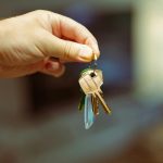 A close-up image of a hand holding a keyring with several house keys, symbolizing real estate and home ownership.